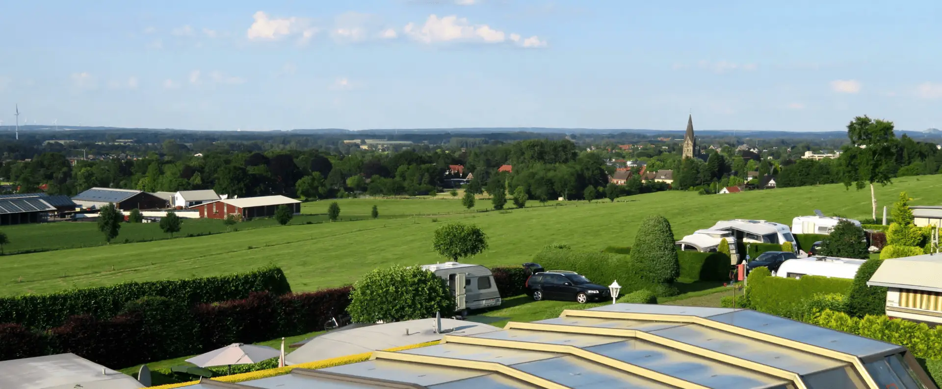 Gruene Landschaft mit Campingwagen und Dorfkirche unter blauem Himmel